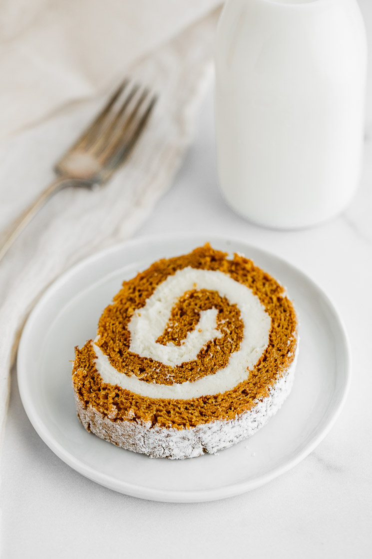 A slice of pumpkin cream cheese roll on a white plate.