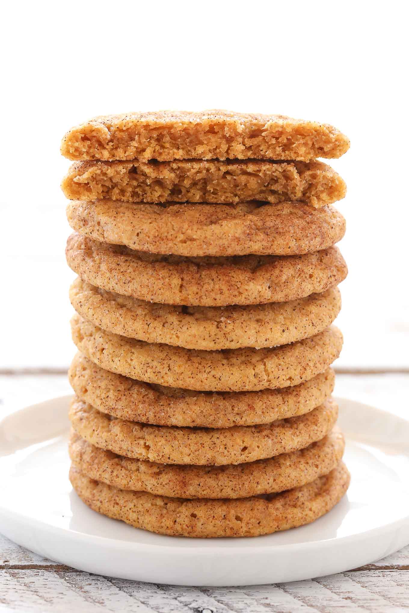 A tall stack of pumpkin snickerdoodles on a white plate. The top cookie has been broken in half. 