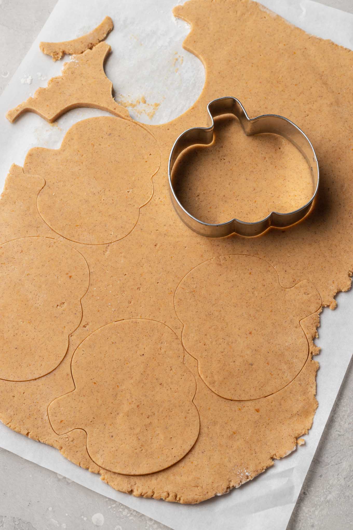 An overhead view of pumpkin cookie dough being cut into pumpkin shapes.