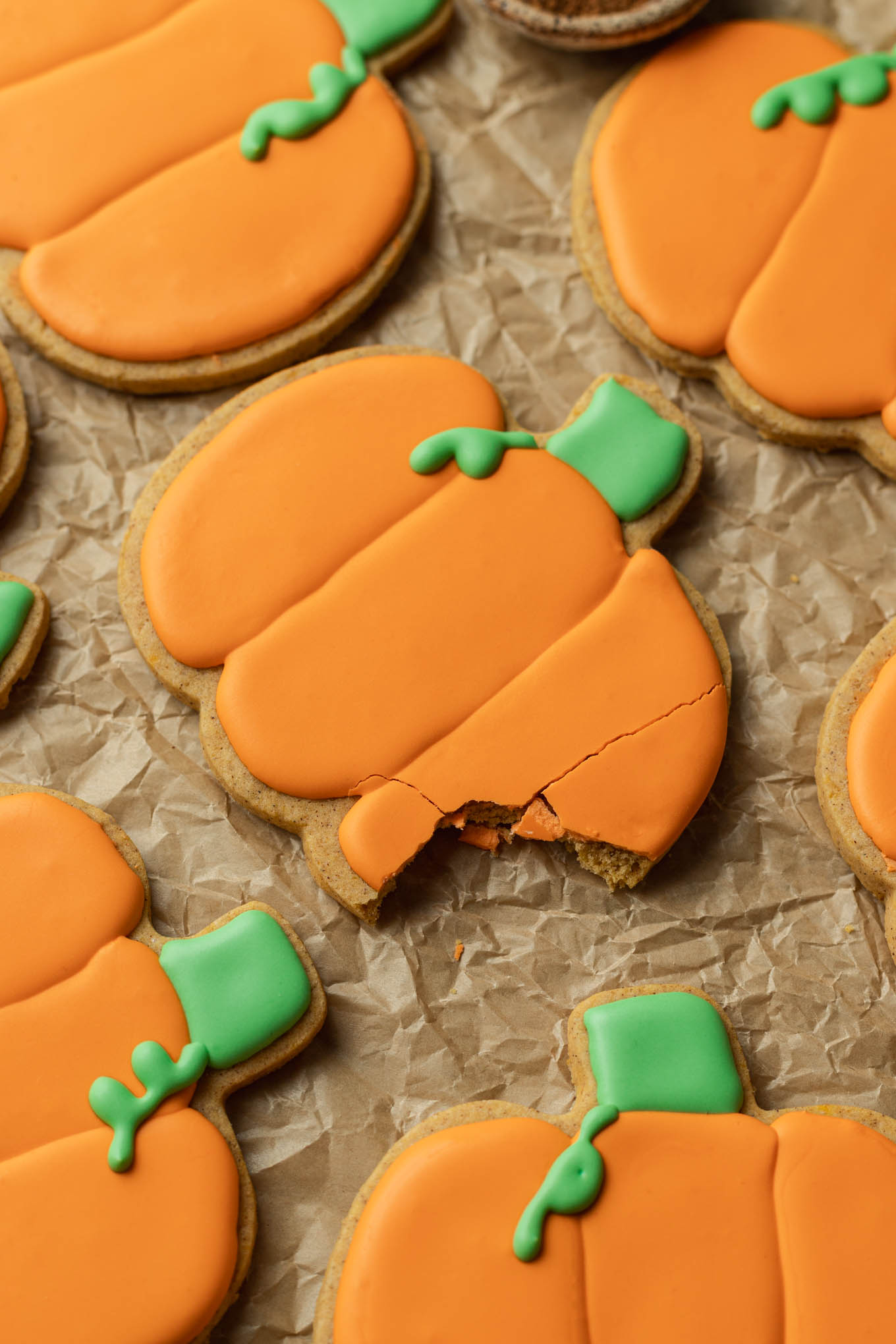 A close-up look at a pumpkin shaped sugar cookie with a bite missing. 