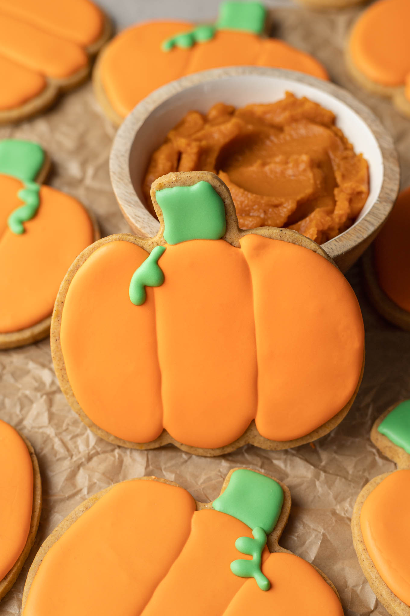 A pumpkin-shaped sugar cookie resting against a small dish of pumpkin puree. 