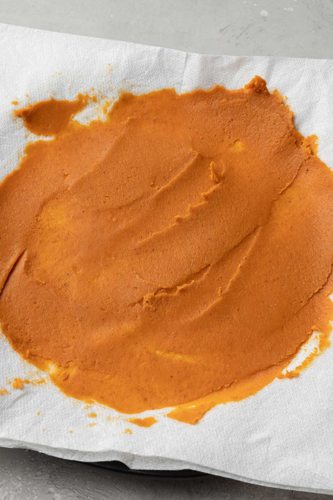 An overhead view of pumpkin puree spread out on paper towels. 