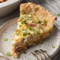 A slice of quiche on a speckled white plate.