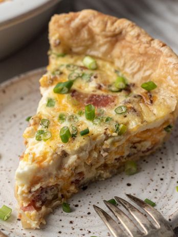 A slice of quiche on a speckled white plate.