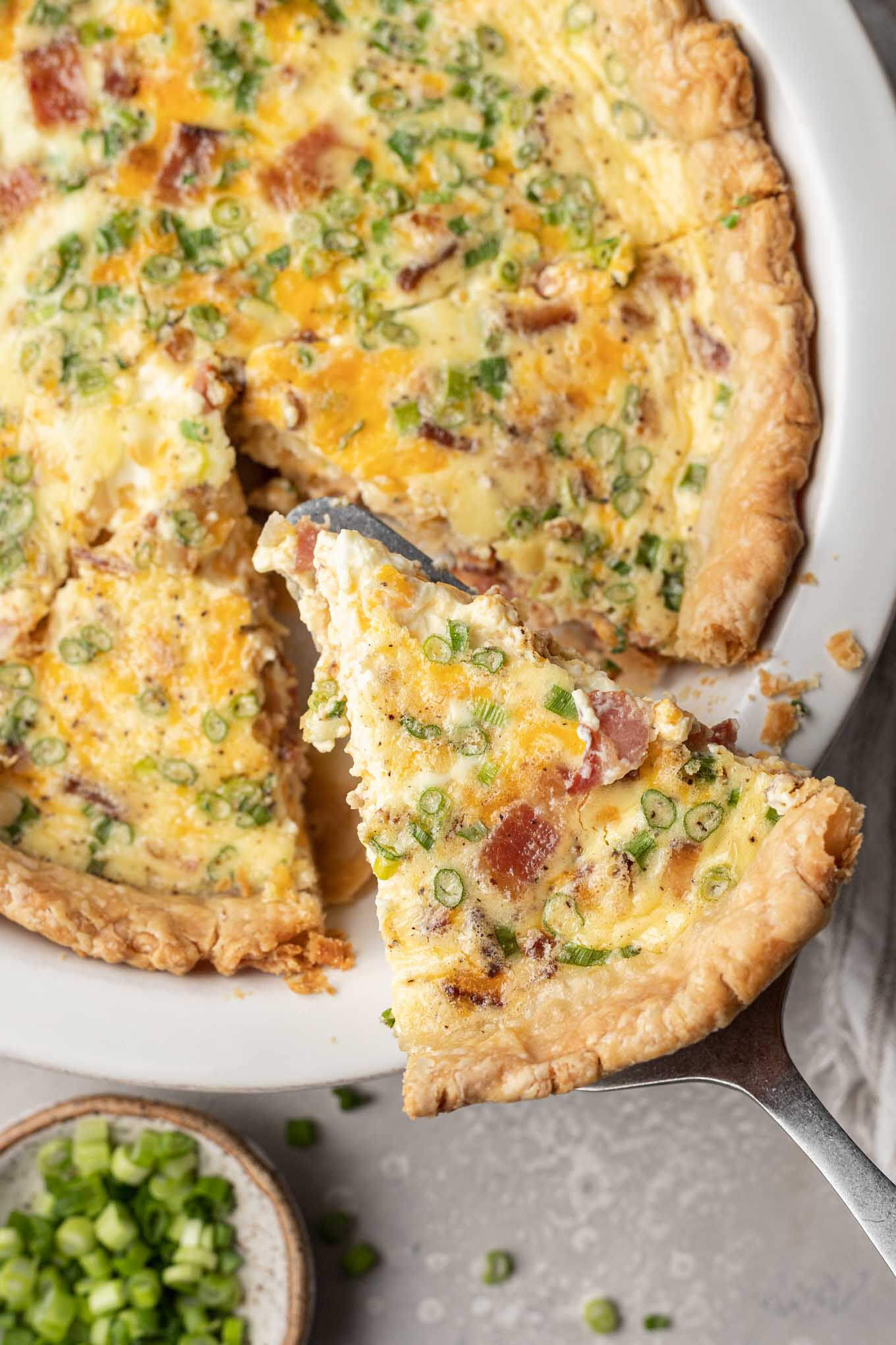 An overhead view of a slice of quiche being removed from a pie plate. 