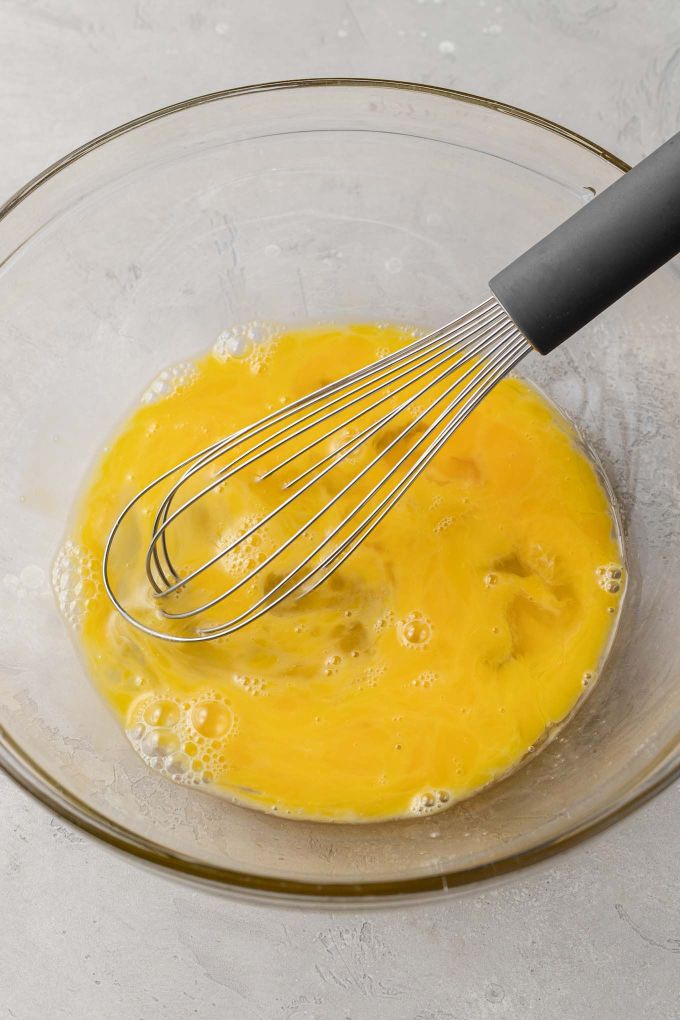 Eggs lightly beaten in a glass mixing bowl.