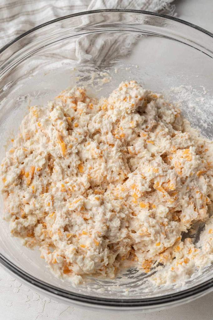 An overhead view of cheddar biscuit dough in a glass mixing bowl.