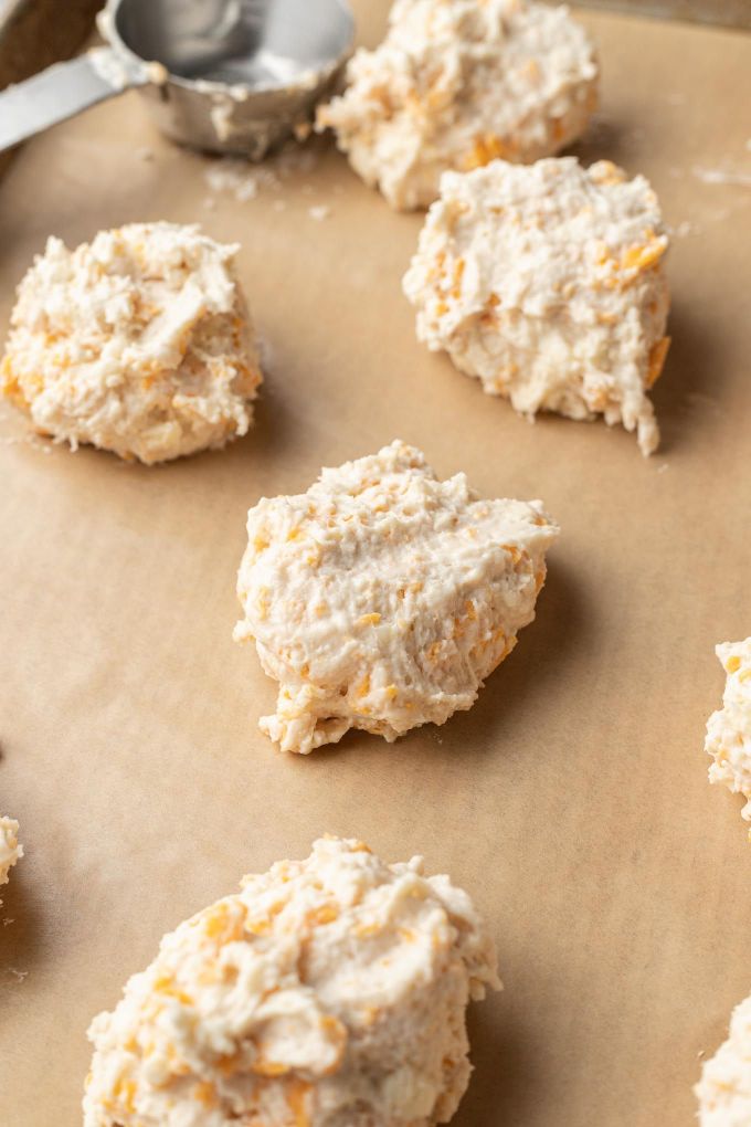 Raw drop biscuit dough on a parchment paper-lined baking sheet.