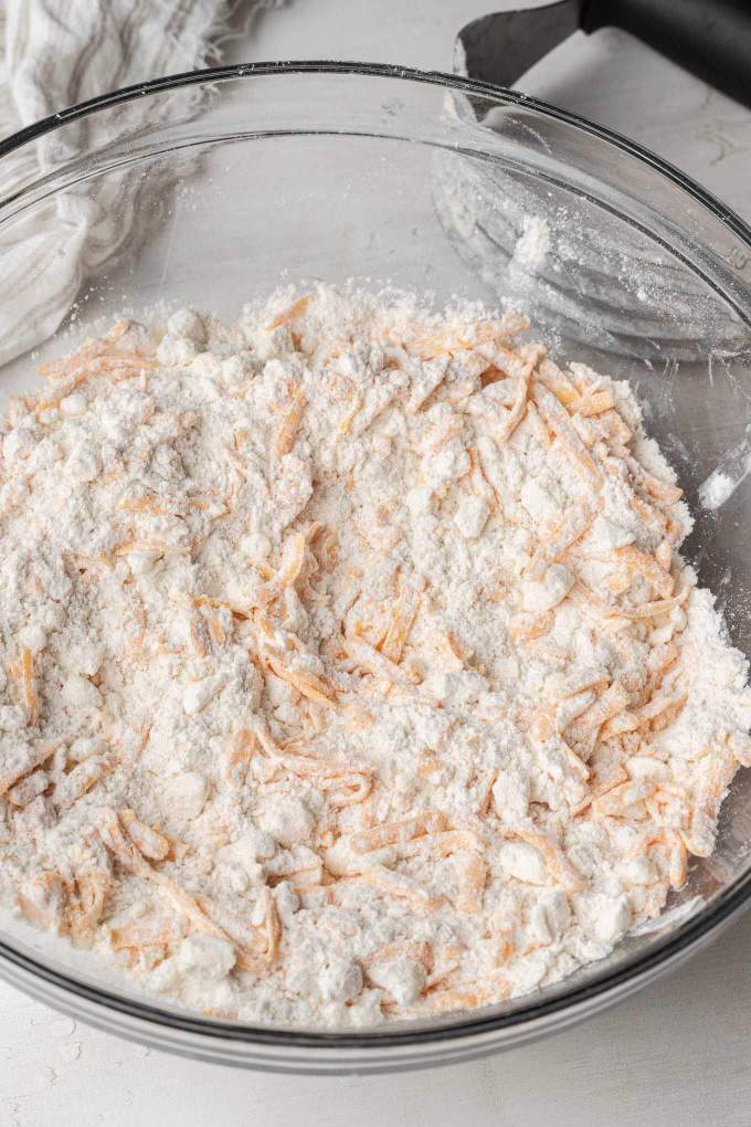 An overhead view of shredded cheddar and dry ingredients in a glass mixing bowl.