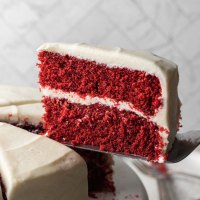A sliced red velvet cake on a cake stand. The slice of cake is being lifted up to show the texture of the cake.