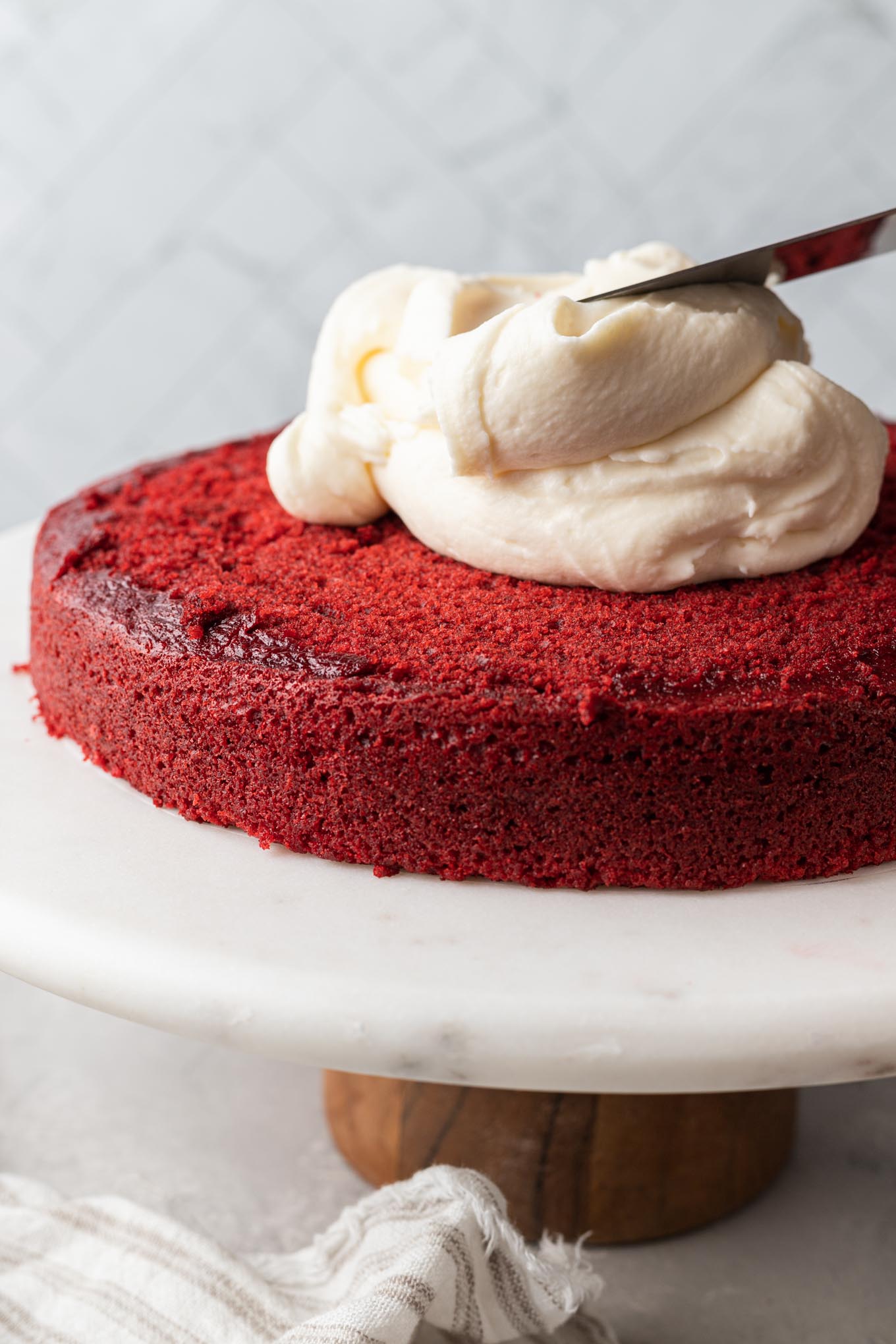 A layer of red velvet cake on a cake stand, being frosted.