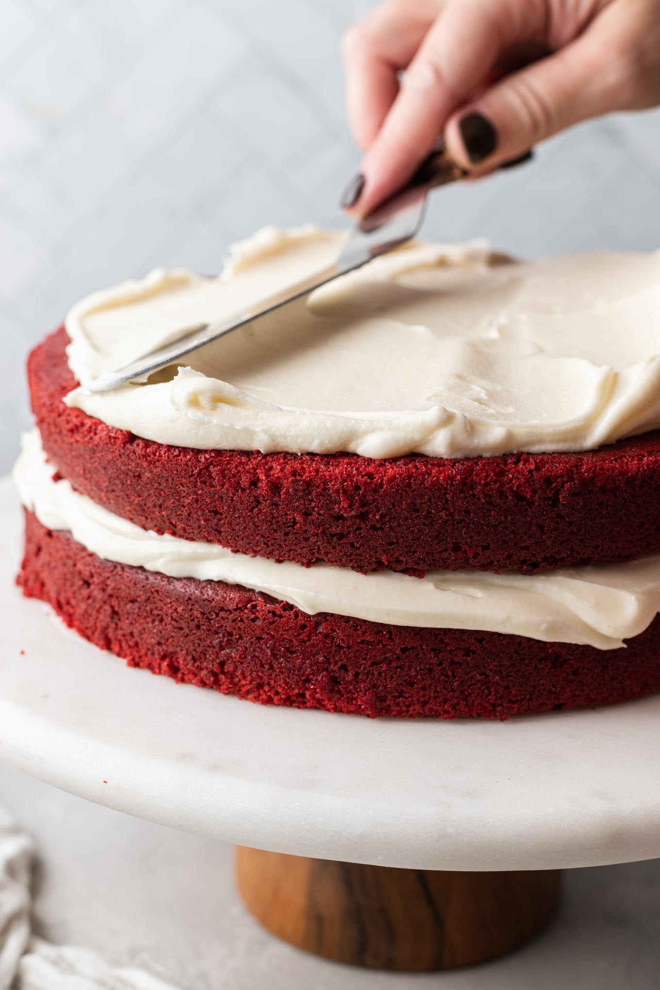 A red velvet layer cake on a cake stand in the process of being frosted.