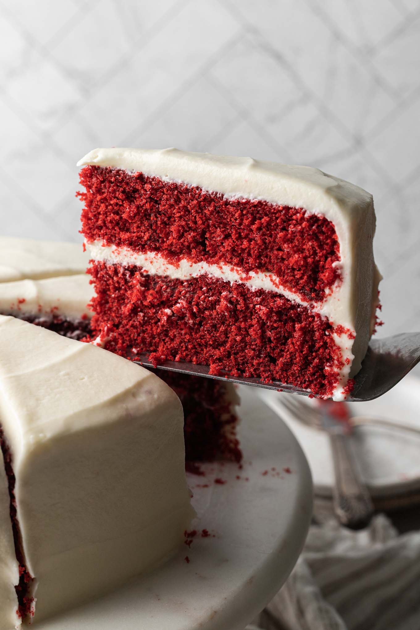 A slice of red velvet cake being served from a cake stand. 