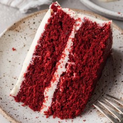 A slice of red velvet cake on a speckled white plate. A fork rests on the plate.