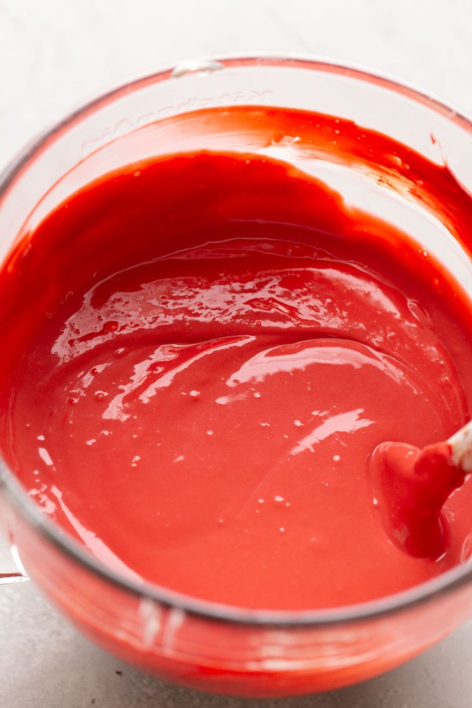 A glass mixing bowl filled with red velvet cake cheesecake batter.