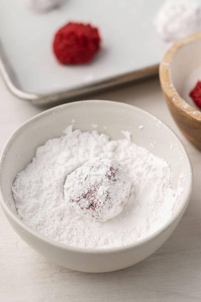 A red velvet cookie dough ball being rolled in powdered sugar. 