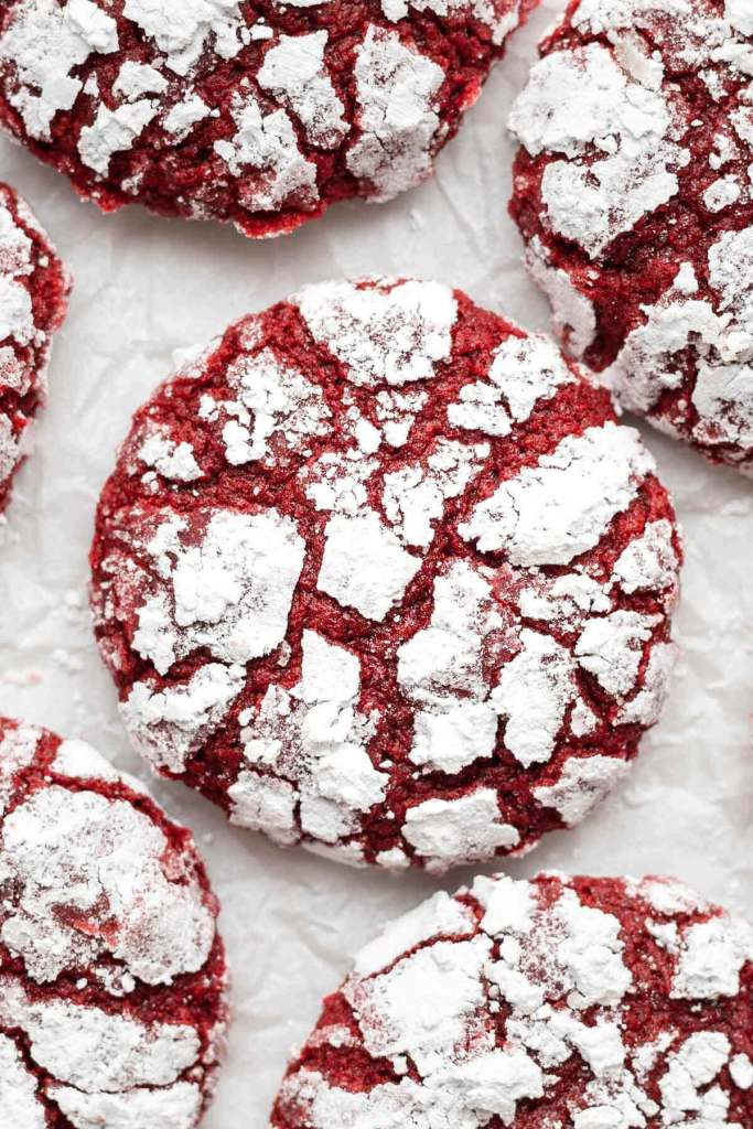 A close up, overhead view of red velvet crinkle cookies on parchment paper. 