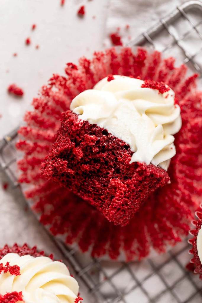 An overhead view of a red velvet cupcake lying on its side. A bite is missing. 