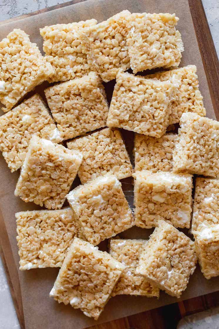 Multiple Rice Krispie treats squares arranged on a wooden tray.