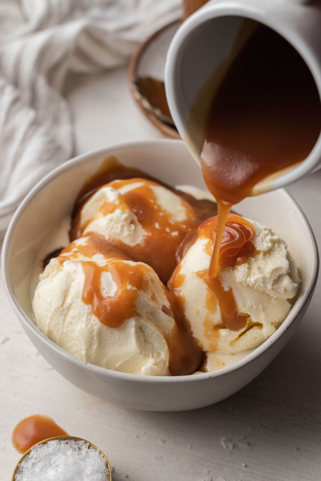 Salted caramel sauce being drizzled over a bowl of vanilla ice cream. 