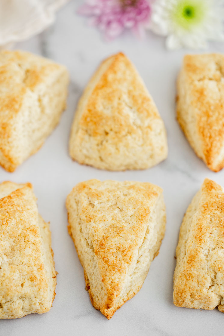 Finished plain scones with a beautiful golden brown crust lined up on a marble surface.