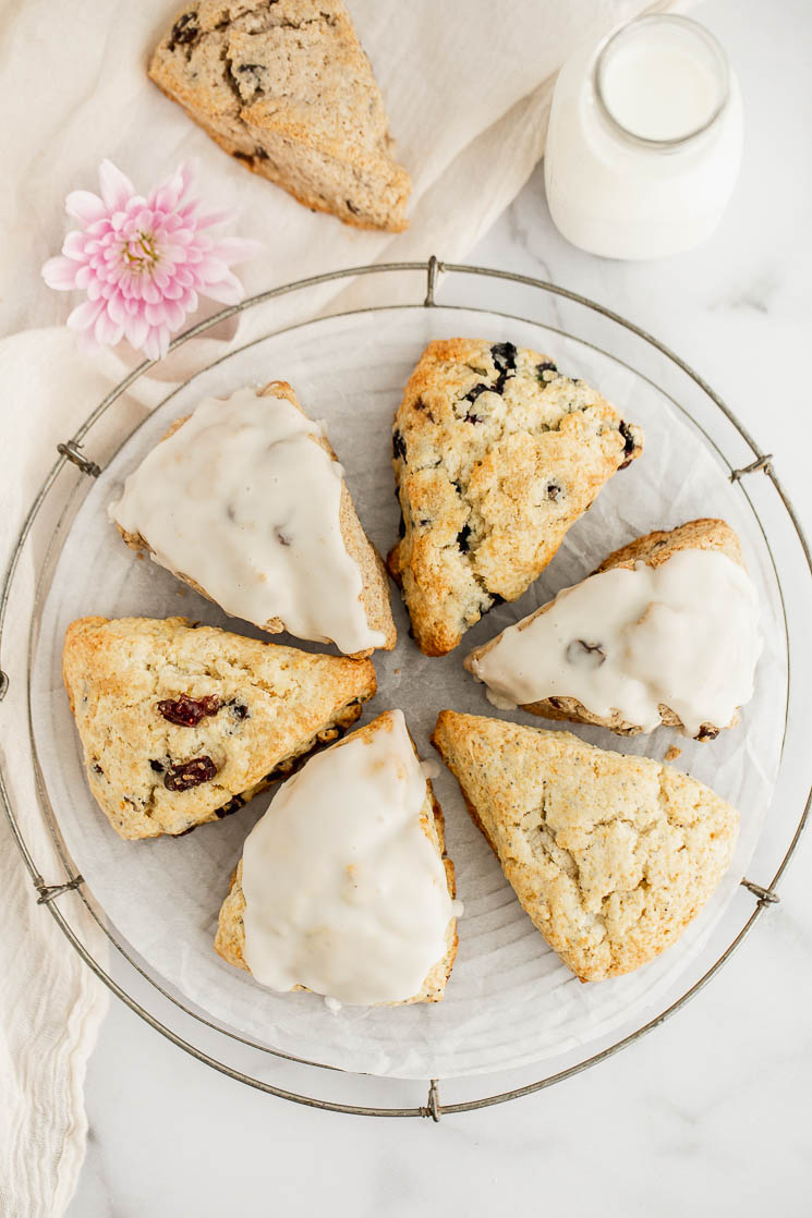 A variety of scones in a circle on a cooling rack with milk and an extra scone in the background.