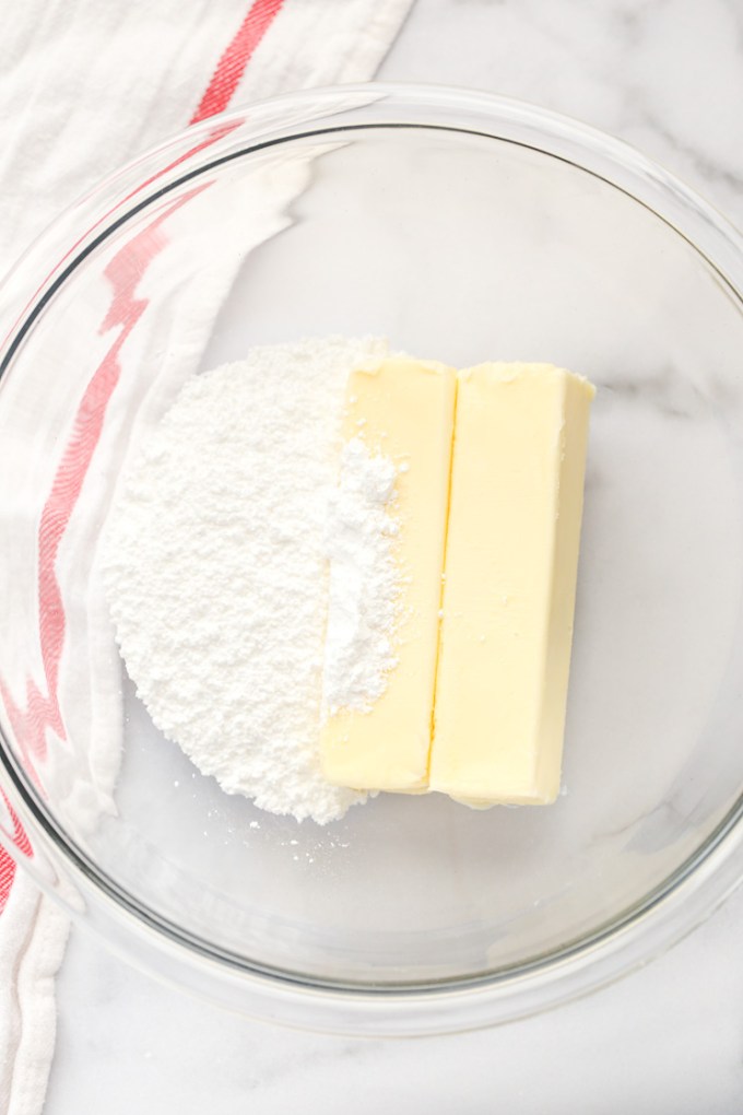 A glass bowl with two sticks of butter and powdered sugar.