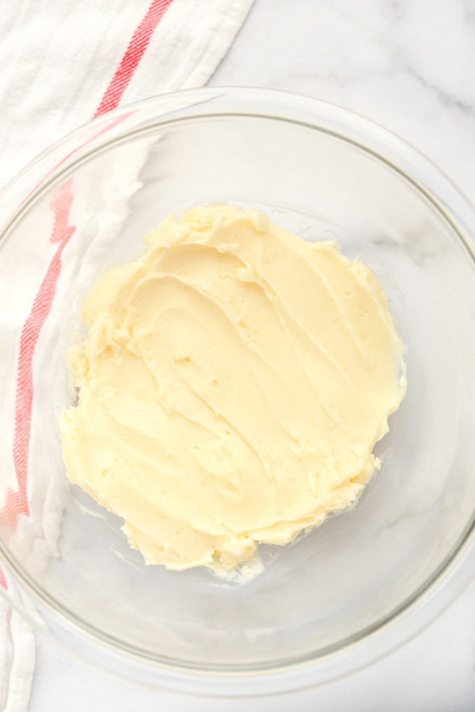 A glass bowl filled with butter that's been mixed together with powdered sugar.