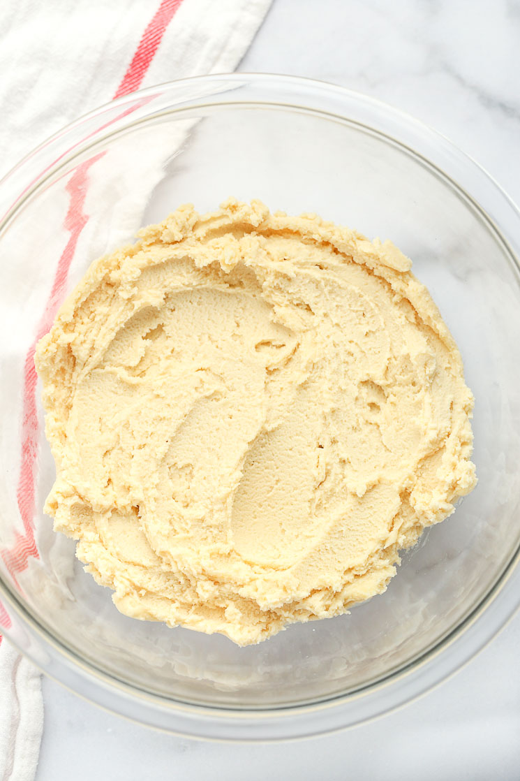 A clear glass mixing bowl filled with shortbread cookie dough and a red and white napkin in the background. 