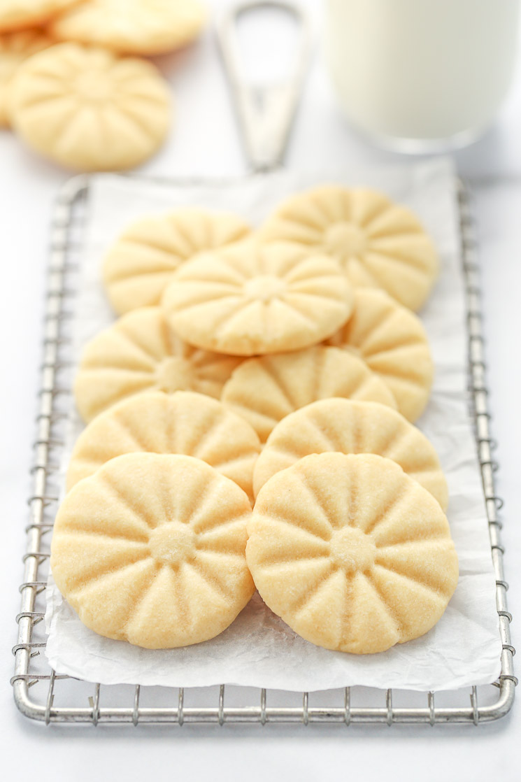 A group of shortbread cookies on top of an antique safety grater with other cookies and milk in the background. 