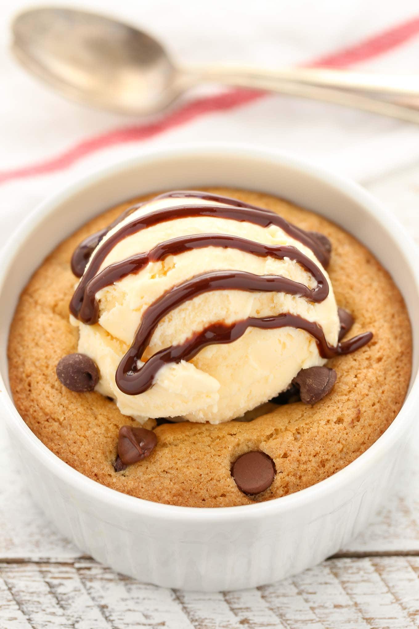 Close up of a deep dish chocolate chip cookie topped with vanilla ice cream and chocolate sauce. 