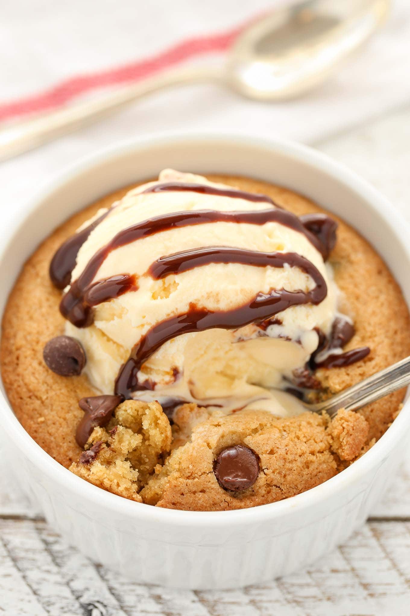 A deep dish single serve chocolate chip cookie topped with ice cream and chocolate sauce. A spoon is being dug into the cookie. 