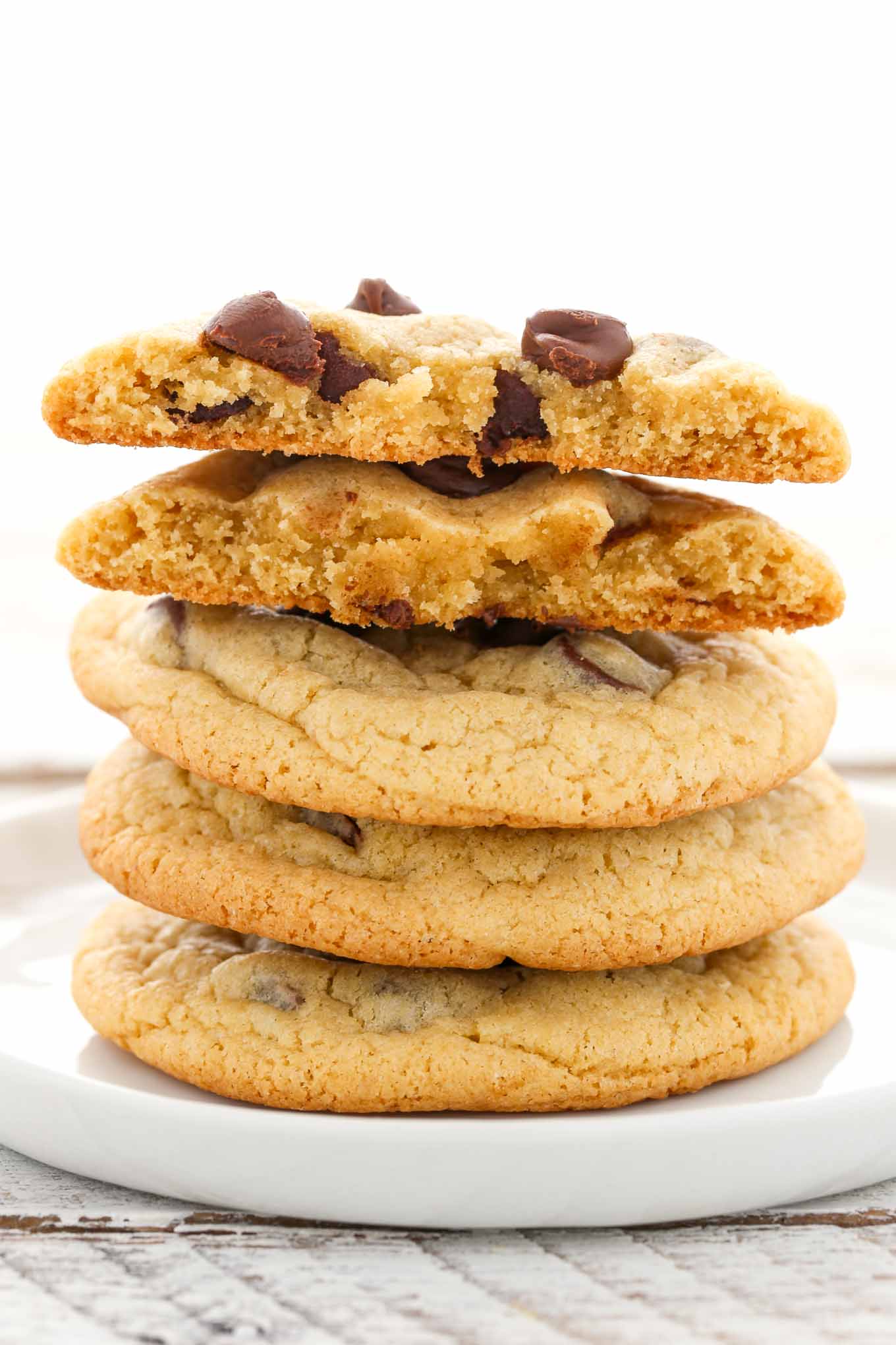 A stack of four chocolate chip cookies on a white plate. 