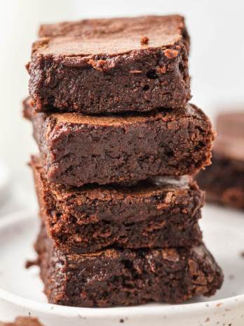 Four brownies stacked on top of each other on a white speckled plate.