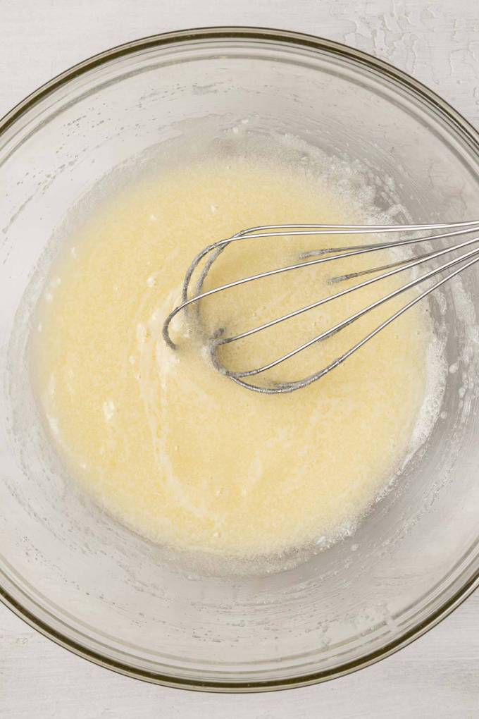 An overhead view of a melted butter-sugar mixture in a glass mixing bowl.