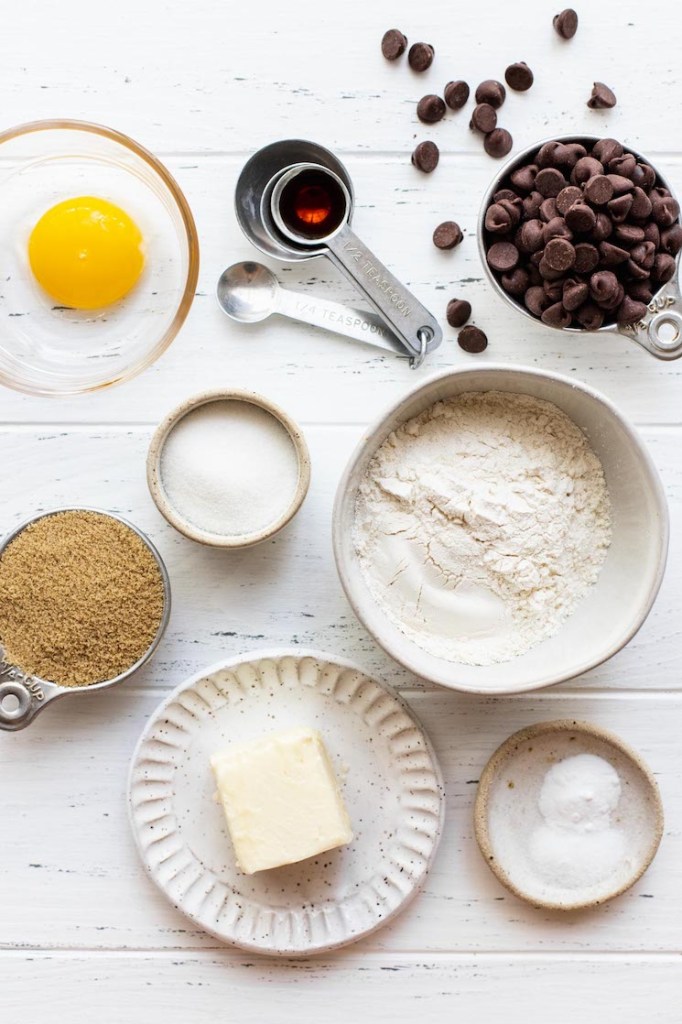 The ingredients needed to make a small batch of chocolate chip cookies sitting on top of a worn white surface.