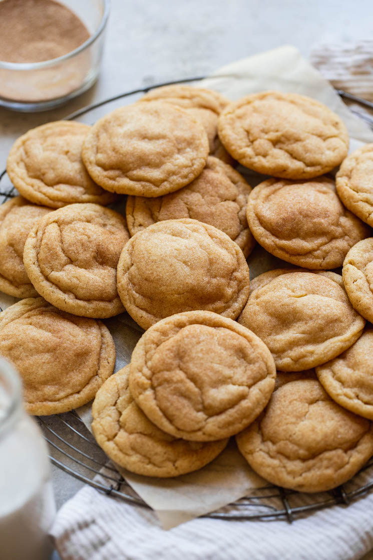 An antique round cooling rack holding a pile of cookies with milk and cinnamon sugar around them.