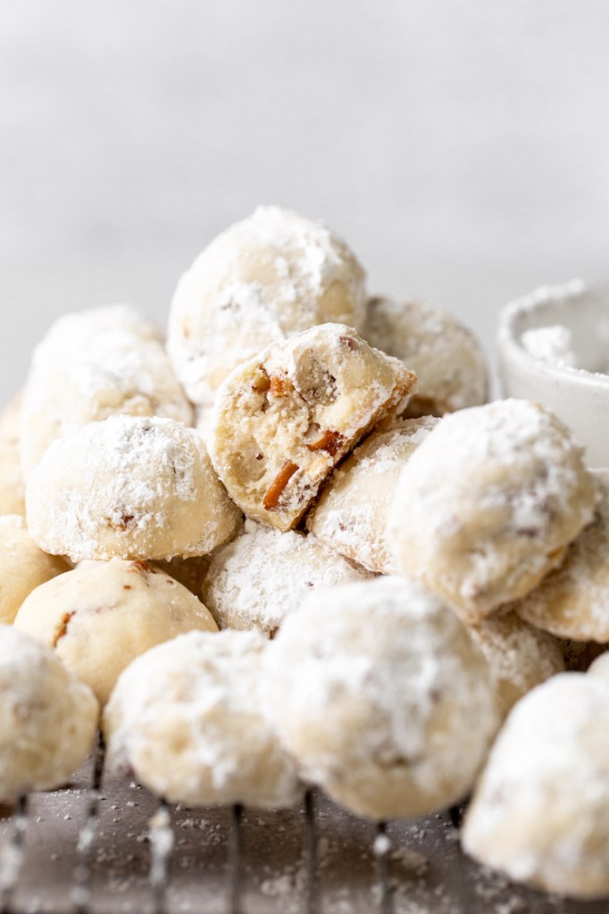 A pile of cookies on a cooling rack with the one in the middle having a bite taken out of it.