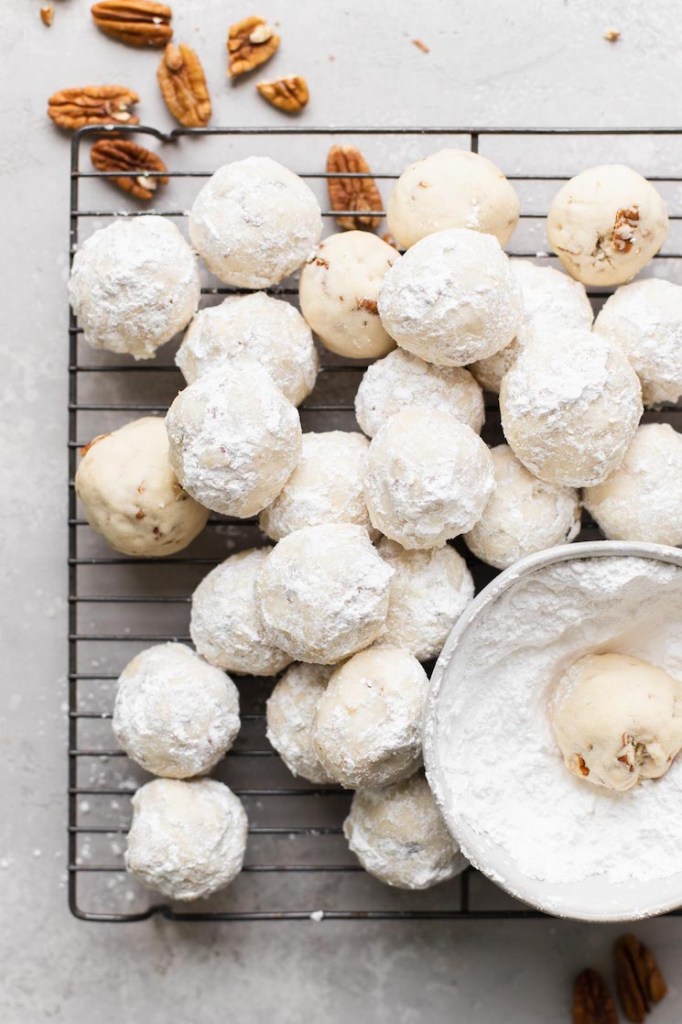 A cooling rack holding a batch of snowball cookies that have been rolled in powdered sugar.