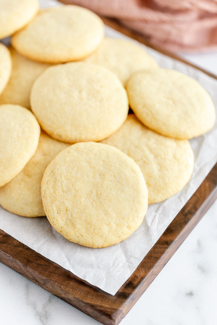 A decorative wood board covered with a stack of sugar cookies.