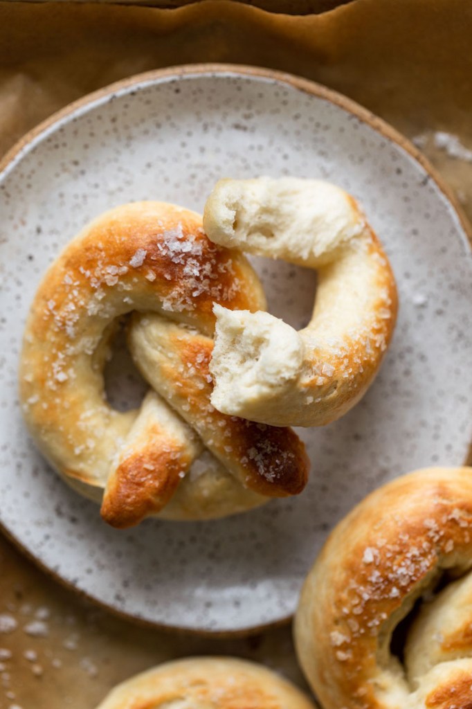 A homemade soft pretzel on a speckled white plate. A piece of the pretzel has been torn off. 