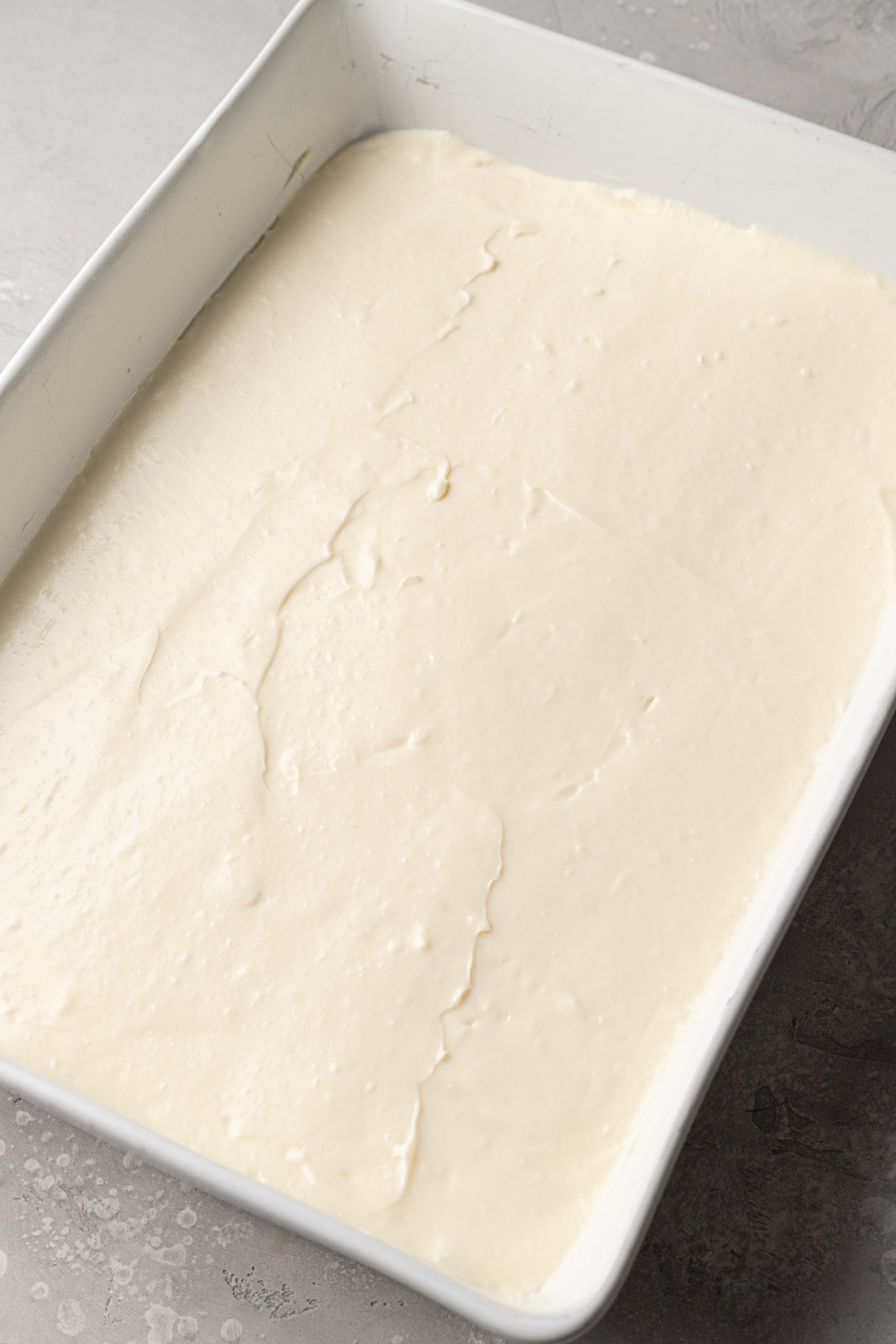 An overhead view of cheesecake filling smoothed into a 9x13-inch pan. 