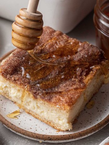 A slice of sopapilla cheesecake being drizzled with honey.