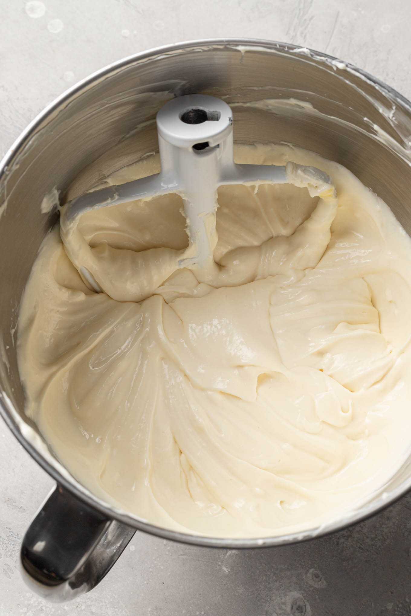 An overhead view of raw cheesecake filling in a mixing bowl, with a paddle attachment. 