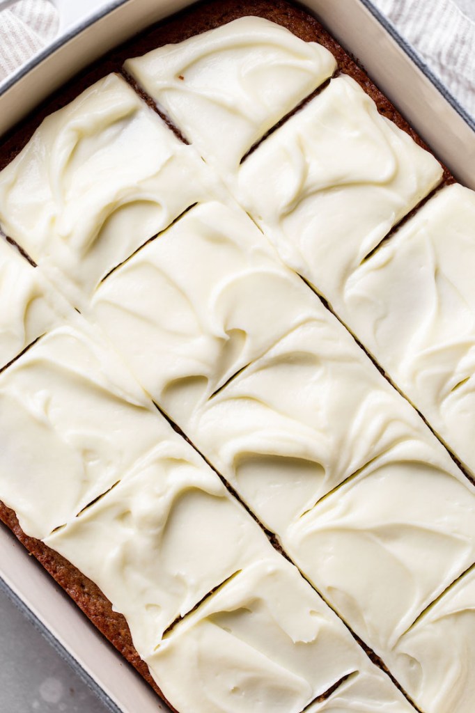 A finished spice cake topped with cream cheese frosting sliced into pieces in the baking pan.