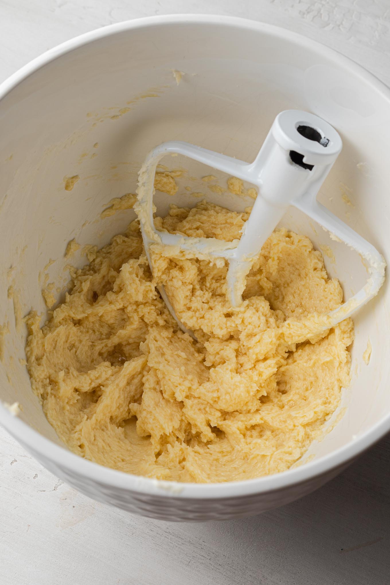 Creamed butter and sugar in a white mixing bowl, with a paddle attachment for a stand mixer.