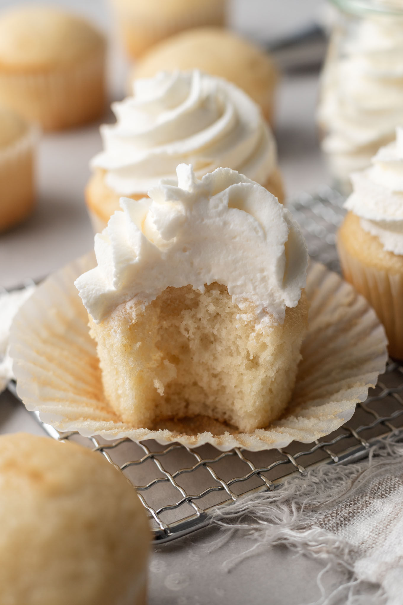 A vanilla cupcake topped with stable whipped cream, with a bite missing. 