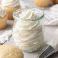 A glass jar filled with gelatin whipping cream. Vanilla cupcakes surround the jar.