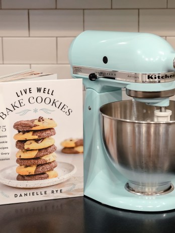 A cookbook sitting next to a blue stand mixer on a black countertop.