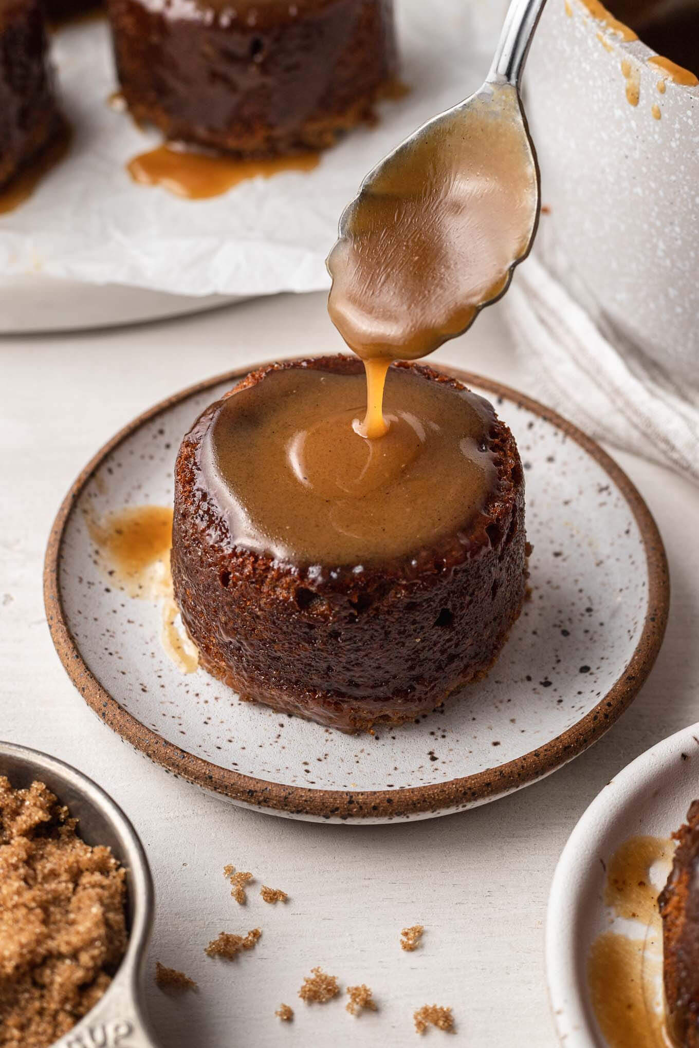 Toffee sauce being spooned over a sticky toffee pudding. 